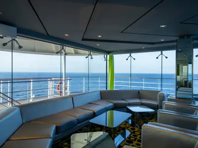Moderne Lounge an Bord der MSC Poesia mit grauen Ledersofas und Glastischen. Große Panoramafenster bieten einen weiten Blick auf das offene Meer und den Himmel.