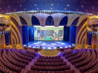 Das opulent gestaltete Teatro Carlo Felice an Bord der MSC Poesia zeigt eine beleuchtete Bühne mit Bühnenbild und zahlreichen lilafarbenen Samtsitzen. Sternenlichter zieren die Decke dieses Theatersaals.