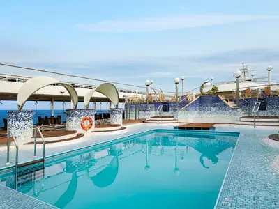 Der weitläufige Poolbereich an Bord der MSC Poesia. Klares, blaues Poolwasser im Vordergrund, umgeben von blauen Mosaikfliesen. Im Hintergrund sind bequeme Liegen, Sitzecken und das offene Meer unter einem weiten Himmel zu sehen.