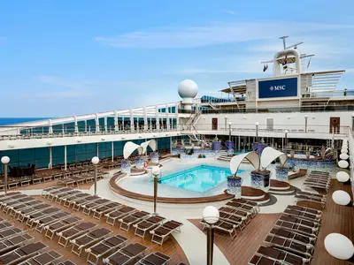 Der grosszügige Aussenpoolbereich der MSC Poesia zeigt hellblaue Pools, Whirlpools und viele braune Liegestühle. Im Hintergrund erstreckt sich das Meer. Ein MSC-Logo prangt auf einer grossen Leinwand.