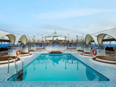 Das Pooldeck der MSC Poesia mit großem Swimmingpool. Dahinter liegen terrassenförmige Whirlpools und eine Meerjungfrauenskulptur. Helles Tageslicht und das Meer am Horizont.