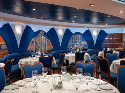 Innenansicht des eleganten "Le Fontane" Restaurants an Bord der MSC Poesia. Zahlreiche Tische sind mit weißen Tischdecken, Gläsern und Geschirr eingedeckt. Blaue Polsterbänke und Holzstühle mit blauen Bezügen prägen das Ambiente. An den Wänden sind künstlerische Wandmalereien mit klassischen Motiven zu sehen, unterbrochen von blauen, fächerförmigen Dekorationen und Wandleuchten.