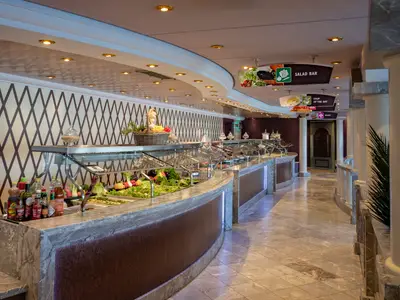 Das helle Buffet-Restaurant an Bord der MSC Poesia zeigt eine lange Theke mit frischen Salaten und warmen Speisen. Elegantes Design mit Marmor, Deckenbeleuchtung. Bereichsschilder sind sichtbar.