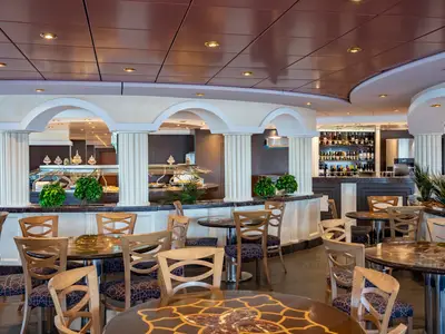 Blick in den Buffetbereich Villa Pompeiana an Bord der MSC Poesia mit Esstischen, Stühlen und Buffetstationen. Klassische Säulen und eine Bar mit Weinflaschen sind sichtbar.