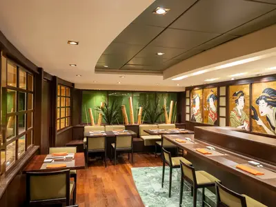 Die Kaito Sushi Bar an Bord der MSC Poesia zeigt elegante Holztische, eine Sushi-Theke und Wandbilder von Geishas. Grüne Pflanzen und Bambusstäbe schmücken den Innenraum.