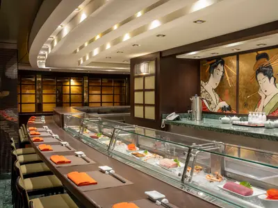 Die Kaito Sushi Bar an Bord der MSC Poesia zeigt eine lange Theke mit Sushi-Auslage, Stühle mit orangefarbenen Servietten und Wandgemälde im japanischen Stil.