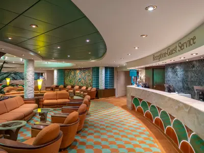 Rezeption und Lounge der MSC Poesia mit geschwungenem Marmortresen und Monitoren. Komfortable orangefarbene Sofas und Sessel auf einem auffälligen, bunten Teppichmuster.