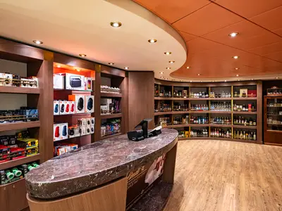 Moderner Duty-Free Shop an Bord der MSC Poesia. Regale mit Elektronik, Spielzeug und Spirituosen sind zu sehen. Eine Marmortheke mit Kasse befindet sich im Vordergrund.