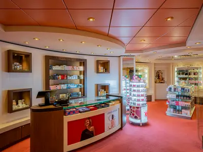 Innenansicht des Duty-Free Parfümerie- und Kosmetikgeschäfts Le Parfum an Bord der MSC Poesia. Parfüms und Make-up-Produkte sind in hellen Regalen und Auslagen präsentiert. Eine Kasse und große Werbeplakate sind sichtbar.