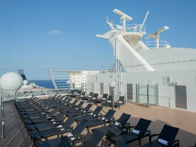 Blick auf das obere Sonnendeck der MSC Poesia mit zahlreichen leeren, dunkelbraunen Sonnenliegen. Im Hintergrund ist das blaue Meer und der klare Himmel zu sehen. Ein Teil des Schiffsaufbaus mit Antennen und Radaranlagen ist rechts im Bild.