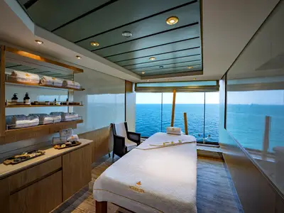 Luxuriöser Spa-Behandlungsraum an Bord der MSC Poesia mit Massageliege und Handtüchern. Ein großes Fenster bietet weiten Meerblick, was eine sehr entspannte Atmosphäre schafft.