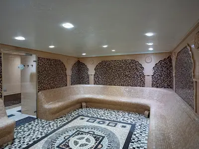 Einladender Thermalbereich im MSC Aurea Spa an Bord der MSC Poesia. Eine gekachelte Sitzbank umgibt den Raum, ergänzt durch Mosaikwände und -boden. Eine Glastür führt zu einem angrenzenden Bereich. Ohne Personen.