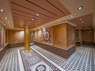 Ein kunstvoll gestalteter Flur im MSC Aurea Spa an Bord der MSC Poesia. Mosaikböden, eine goldene Mosaiksäule und Wandpaneele prägen den Bereich. Indirekte Deckenleuchten erhellen den eleganten Raum.