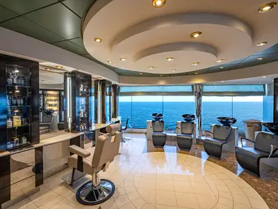 Ein heller Friseursalon an Bord der MSC Poesia mit großen Fenstern zum Meer. Mehrere Friseurstühle und Haarwaschbecken sind zu sehen. Die Decke ist modern mit Einbaulampen gestaltet.