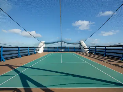 Ein leerer, teal-farbener Multi-Sportplatz mit weissen Linien an Deck der MSC Poesia. Hohe Netze umgeben den Platz, der von einem blauen Himmel und dem weiten Meer umrahmt wird.