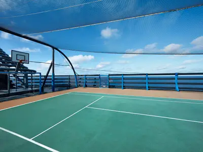 Multifunktionssportplatz an Deck der MSC Poesia. Grüner Boden, weiße Linien, Basketballkorb und Fußballtor unter Schutznetz. Im Hintergrund weites Meer unter blauem Himmel.