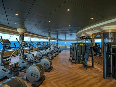 Ein modernes Fitnesscenter an Bord der MSC Poesia, ausgestattet mit Technogym Geräten wie Crosstrainern und Kraftstationen. Große Fenster bieten einen weiten Blick auf das offene Meer.