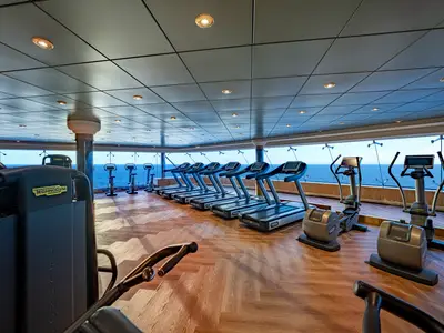 Ein modernes Fitnessstudio an Bord der MSC Poesia mit einer Reihe von Technogym-Laufbändern und Ellipsentrainern. Große Fenster bieten einen Panoramablick auf das weite Meer.