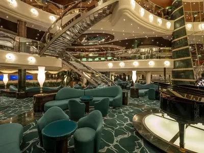 Das prunkvolle Atrium der MSC Preziosa mit geschwungenen Treppen, türkisgrünen Sitzgruppen, Rezeption und einem schwarzen Flügel.