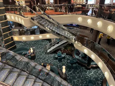 Blick von oben in das glamouröse Atrium an Bord der MSC Preziosa mit geschwungenen, funkelnden Kristalltreppen und blauen Sitzgruppen.