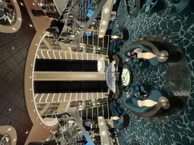 Ein Blick von oben auf das luxuriöse Atrium an Bord der MSC Preziosa mit grünen Sitzecken, einem Flügel und glänzenden Treppenaufgängen.