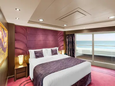 Eine elegant eingerichtete Balkonkabine an Bord der MSC Preziosa mit einem Doppelbett, lila Akzenten, Nachttischlampen und direktem Meerblick durch eine große Glastür zum Balkon.