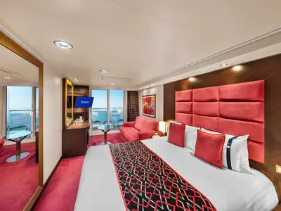 Geräumige Balkonkabine an Bord der MSC Preziosa. Sie verfügt über ein großes Doppelbett, eine rote Couch, einen Schreibtisch mit TV und einen privaten Balkon mit Meerblick.