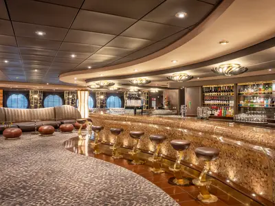 Luxuriöse Safari Lounge an Bord der MSC Preziosa. Geschwungene Bar mit Hockern und Sitzecke mit Sofas. Im Hintergrund, hinter der Theke, Regale voller Spirituosen und Weine.