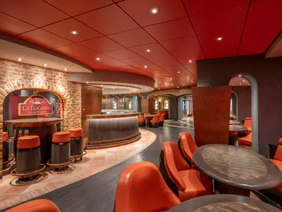 Innenansicht des La Locanda Pizzeria Wine Bar an Bord der MSC Preziosa, mit orangen Sesseln, Holztischen, Ziegelwänden und einer stilvollen Bar. Die rote Decke und warmes Licht schaffen eine einladende Atmosphäre.