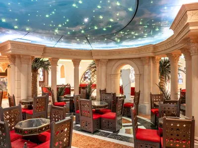Die Phoenician Plaza Lounge an Bord der MSC Preziosa. Tische und Stühle im orientalischen Stil, umgeben von Säulen und Palmen unter einer leuchtenden Sternenhimmel-Decke.
