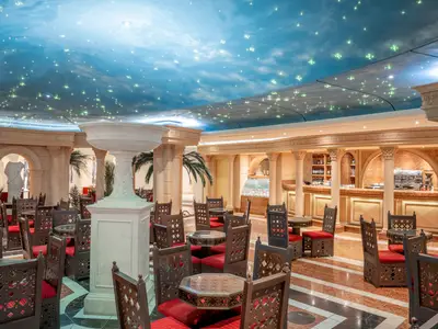 Elegante Bar-Lounge an Bord der MSC Preziosa. Mit Sternenhimmel-Decke, klassischen Säulen und orientalischen Tischen und Stühlen. Eine Bar ist im Hintergrund sichtbar.