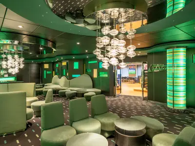 The Green Sax Bar auf der MSC Preziosa. Grüne Sitzmöbel, beleuchtete Wände und Kugel-Kronleuchter schaffen modernes Flair. Ein angrenzender Raum ist sichtbar.