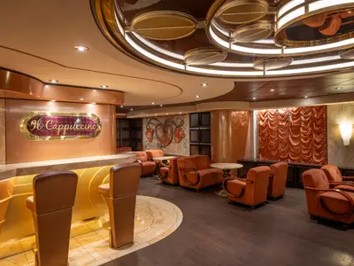 Die elegante Il Cappuccino Bar an Bord der MSC Preziosa. Sichtbar sind ein goldener Tresen mit Barhockern, bequeme orange Samtsessel und eine markante Deckenbeleuchtung.