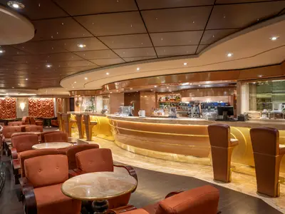 Die stilvolle Bar Il Cappuccino an Bord der MSC Preziosa zeigt eine lange, beleuchtete Theke mit Hockern und bequeme Sessel mit kleinen Tischen. Eine elegante Innenansicht.