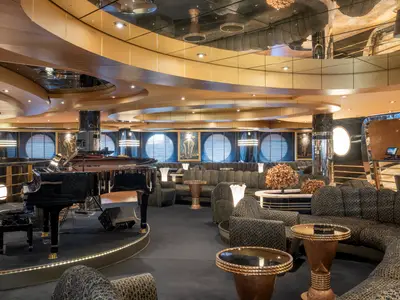 Elegante Bar-Lounge an Bord der MSC Preziosa mit schwarzem Flügel auf erhöhter Bühne, bequemen Sitzgruppen in dunklem Muster und runden Fenstern.