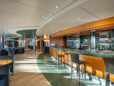 Elegante Bar La Playa Preciosa an Bord der MSC Preziosa. Grüne Marmortheke, Holzverkleidung, volle Spirituosenregale und moderne Sitzgruppen im hellen Innenbereich.