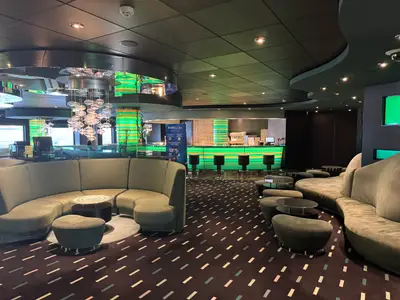 Eine modern gestaltete Lounge an Bord der MSC Preziosa mit geschwungenen grünen Sofas, stilvoller Beleuchtung und einer Bar im Hintergrund.