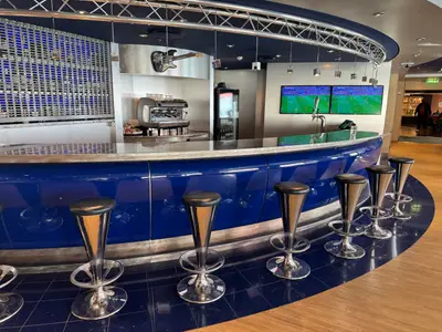 Blick auf die geschwungene blaue Bar mit silbernen Barhockern in der Sports Bar an Bord der MSC Preziosa.
