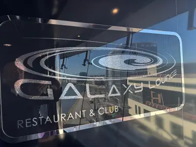 Ein graviertes Glasschild der Galaxy Lounge an Bord der MSC Preziosa mit Blick auf den Hafen im Hintergrund.