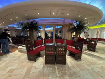 Eine Lounge im italienischen Stil an Bord der MSC Preziosa mit Säulen, Palmen, roten Sitzpolstern und verzierten Holzstühlen.