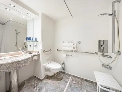 Helles, barrierefreies Badezimmer an Bord der MSC Preziosa. Es verfügt über eine begehbare Dusche mit Klappsitz, Haltegriffe und eine wandhängende Toilette. Der Waschtisch und der Boden sind aus Marmor.