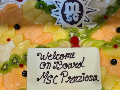Eine kunstvoll verzierte Torte mit frischen Früchten und einem Schild mit der Aufschrift 'Welcome On Board MSC Preziosa'.