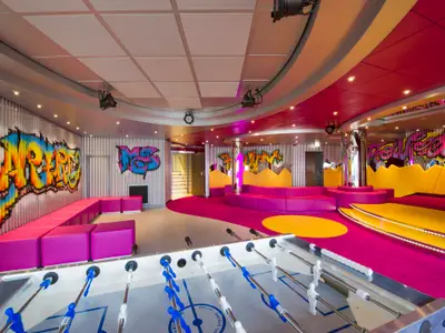 Der farbenfrohe Graffiti's Teens Club an Bord der MSC Preziosa mit neonfarbenen Möbeln, Streetart an den Wänden und einem Tischkicker im Vordergrund. Der Raum ist hell beleuchtet und modern gestaltet.