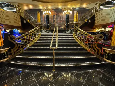 Eine prachtvolle, symmetrische goldene Treppe mit beleuchteten Stufen im Casino an Bord der MSC Preziosa.