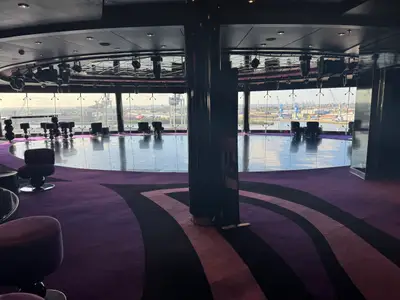 Blick in die moderne Lounge an Bord der MSC Preziosa mit lila Teppich, Tanzfläche und großen Fenstern zum Hafen.