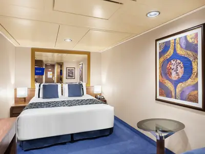 Komfortable Innenkabine an Bord der MSC Preziosa mit Doppelbett, Nachttischen, Spiegel und abstraktem Kunstwerk. Blauer Teppichboden. Modern und einladend gestaltet.