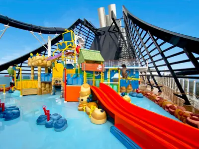 Der farbenfrohe Doremi Castle Aquapark an Bord der MSC Preziosa zeigt helle Böden, rote Wasserrutschen und thematische Spielstrukturen wie Piratenschiff und Dschungelhöhle unter blauem Himmel. Keine Personen.