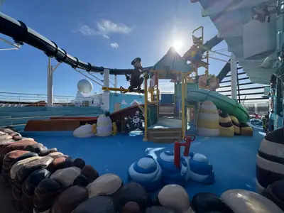 Bunter Kinder-Wasserspielplatz mit Rutschen und Piratendekoration an Bord der MSC Preziosa unter blauem Himmel.