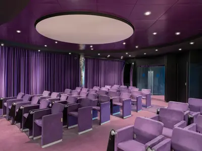 Der Konferenzraum an Bord der MSC Preziosa ist lila: Sessel, Teppich, Vorhänge. Eine große runde Deckenleuchte und Spots erhellen den Raum.