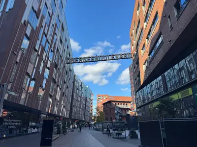 Ein Landausflug der MSC Preziosa führt zum Hamburger Überseeboulevard mit modernen Backsteingebäuden unter blauem Himmel.